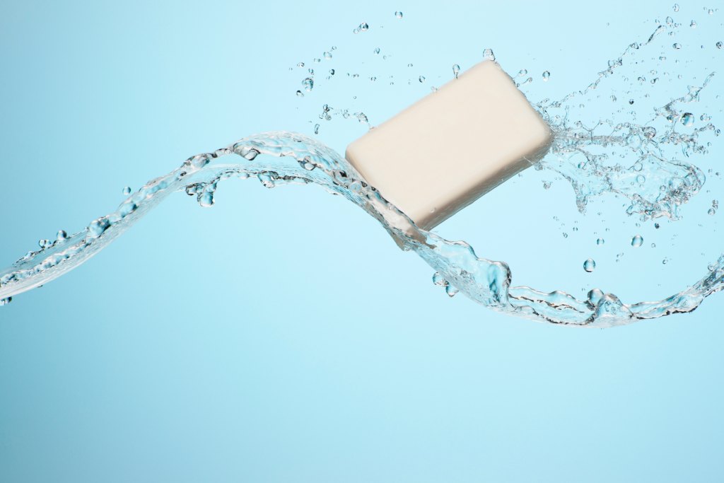 Big flowing splash of clean refreshing water with a white bar of soap in studio on a light blue background 