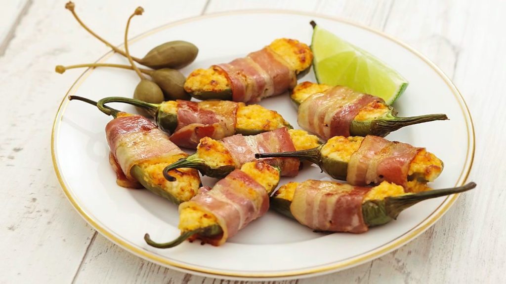 Bacon-Wrapped Stuffed Jalapeños sits on a white plate (air fryer appetizers )