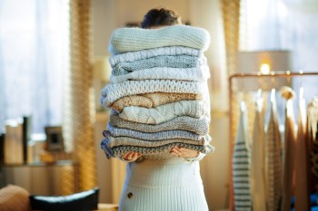 Woman in modern house in sunny winter day holding a pile of sweaters.