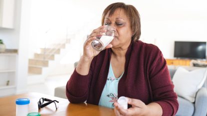 mature woman taking a pill drinking water, feeling sick, covid-19 recovery concept