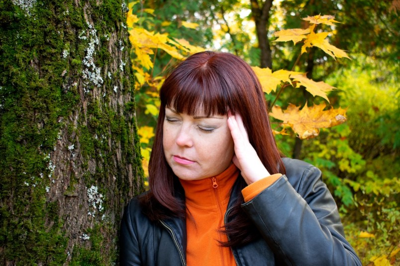 Woman with headache standing by tree