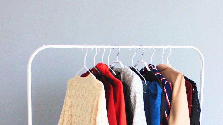 A white clothing rack filled with brightly colored fall sweaters and jackets.