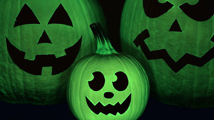 Three pumpkin faces painted with glow-in-the-dark green spray paint.