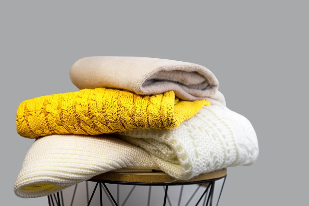 Stack of Trendy Bright illuminating Yellow and White Woolen Knitted Sweaters on Gray Background. (how to fold a sweater)