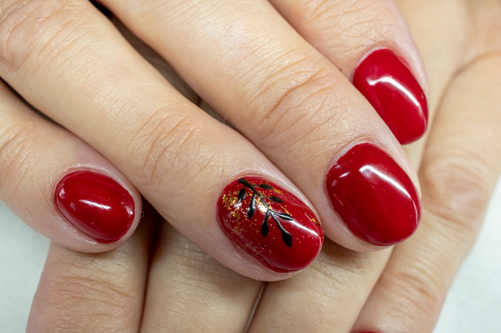 Red nails with black leaf design on ring fingernail.