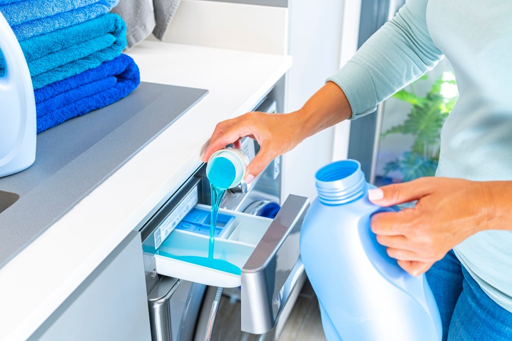 Close up of woman hands adding fabric softener or detergent to a modern washing machine. (get rid of washing machine smell )