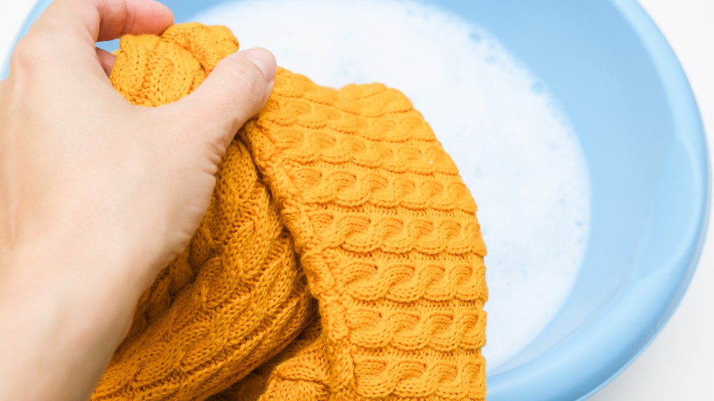 Woman hand-washing yellow crochet blanket in a basin of soapy water