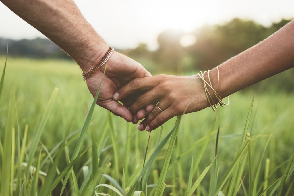 Pisces and Aquarius Compatibility: Shot of romantic couple holding hands in a field. 
