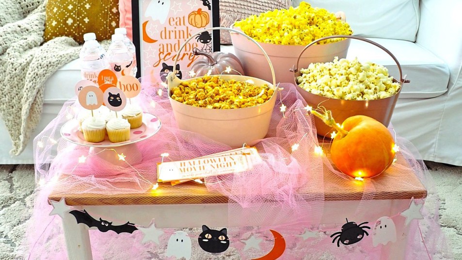 Halloween Movie Night: A low-profile table set with popcorn, twinkle lights, pumpkins and movie night snacks