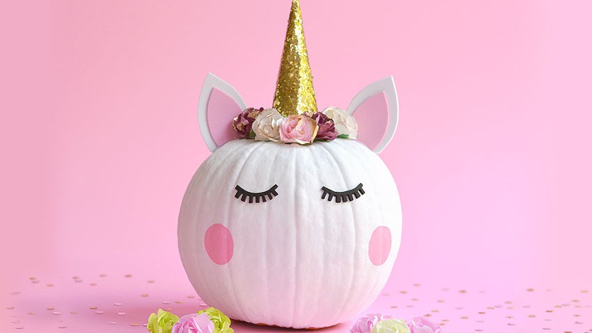White pumpkin face decorated to look like a unicorn with sparkly gold foam horn and foam ears