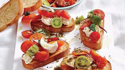 tomato caper bruschetta recipe: crostinis on serving board with tomatoes