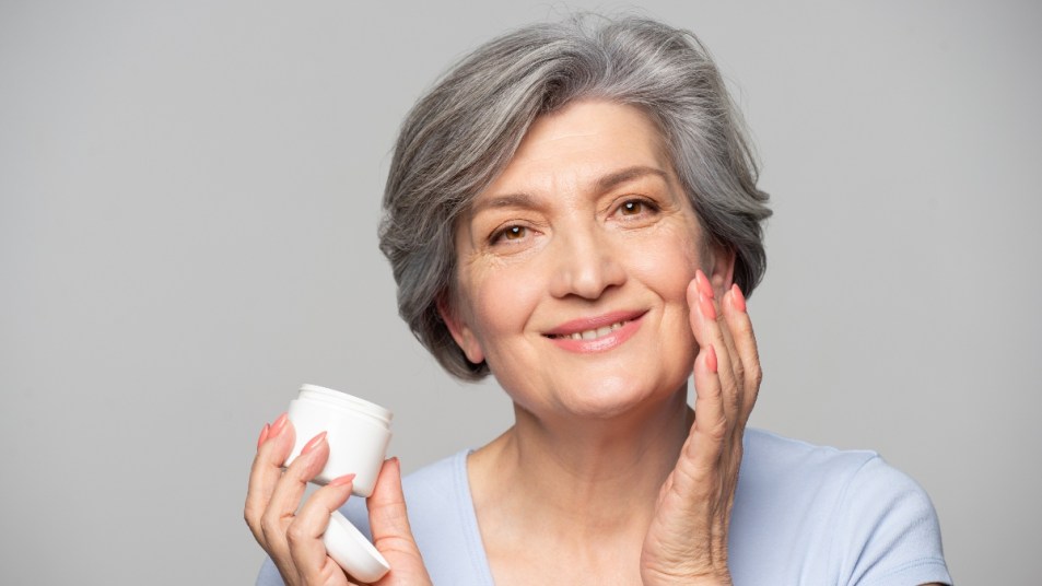 mature woman applying facial cream to her skin as a treatment