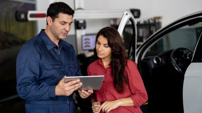 Friendly mechanic showing female customer the work done on her car on tablet at the car workshop both smiling