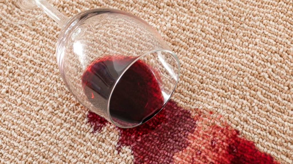 How to get wine stains out: Home mishap and domestic accident concept with close up of a spilled glass of red wine on brown carpet