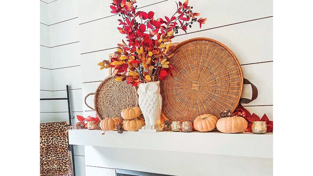 Fall mantel decor ideas: White fireplace mantel decorated in a boho chic style with oversized baskets, pumpkins, a white owl vase filled with colorful leaves and candle cups.
