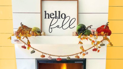 Fall mantel decor ideas: White fireplace mantel decorated in a modern luxe style with velvet pumpkins, a festive framed sign, a wood bead garland and colorful candlesticks.
