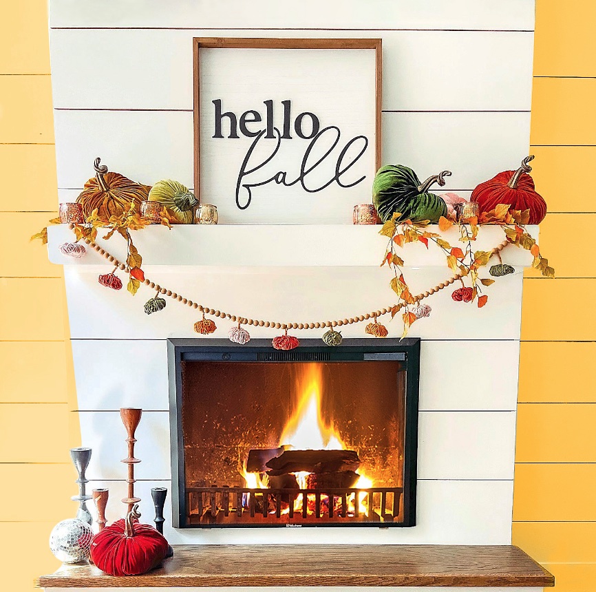 Fall mantel decor ideas: White fireplace mantel decorated in a modern luxe style with velvet pumpkins, a festive framed sign, a wood bead garland and colorful candlesticks.