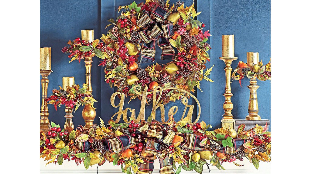 Fall mantel decor ideas: Fireplace mantel decorated with traditional colorful leafy garland and wreath, gold candlesticks and gold "gather" sign.