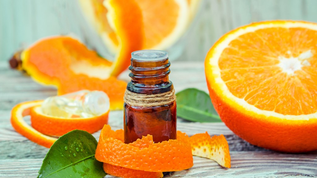 Orange essential oil bottle surrounded by halved oranges and orange peels
