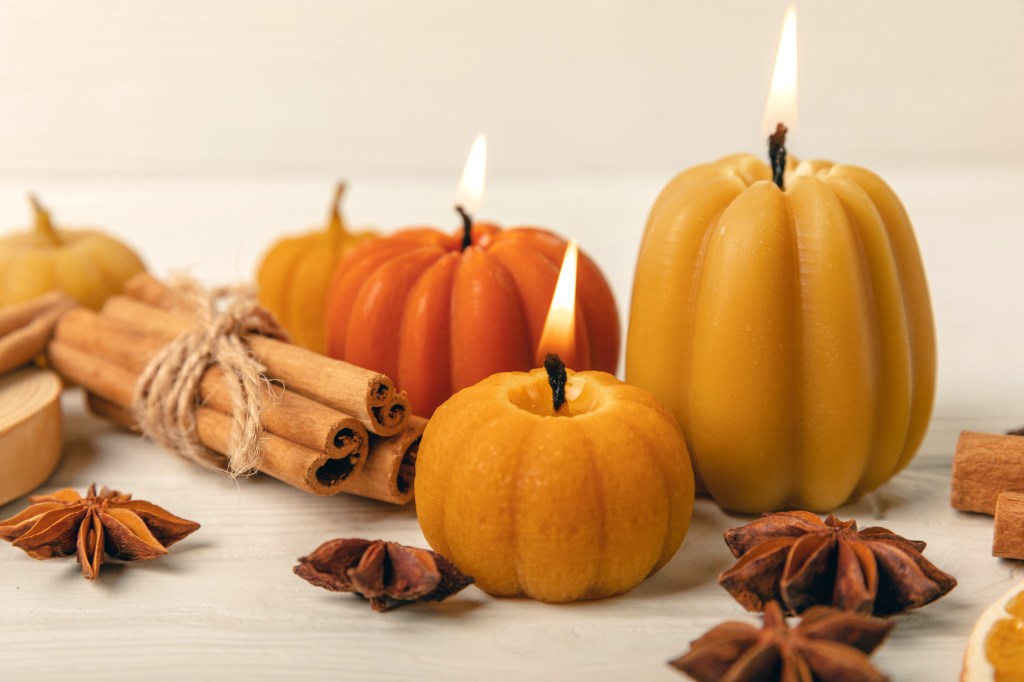 Pie party: Collection of pumpkin-shaped candles surrounded by autumnal leaves and cinnamon sticks on tabletop
