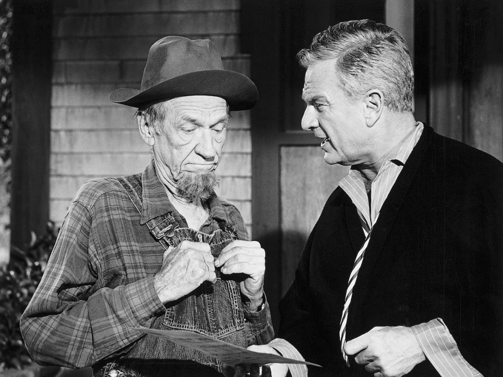 Eddie Albert and Hank Patterson. (Original Caption) A scene from the long-running television series "Green Acres." The series, which ran from 1965-1971, starred Eva Gabor as "Lisa Douglas," and Eddie Albert as "Oliver Douglas." In this scene, Oliver Douglas speaks with his farmer neighbor, Hank Patterson as "Fred Ziffel." Douglas holds a document in his hand; the two are shown from the waist-up. Publicity handout, ca. 1965-1971.