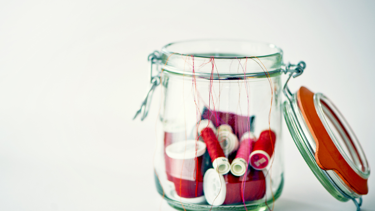 empty candle jar holding sewing thread