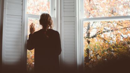 woman staring out window at fall leaves