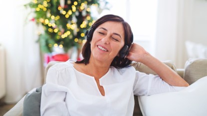 Woman with eyes closed listening to headphones with Christmas decor in background