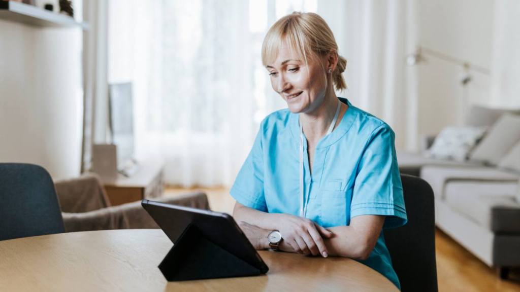 work from home nursing jobs: Female nurse on video call with digital tablet at home.
