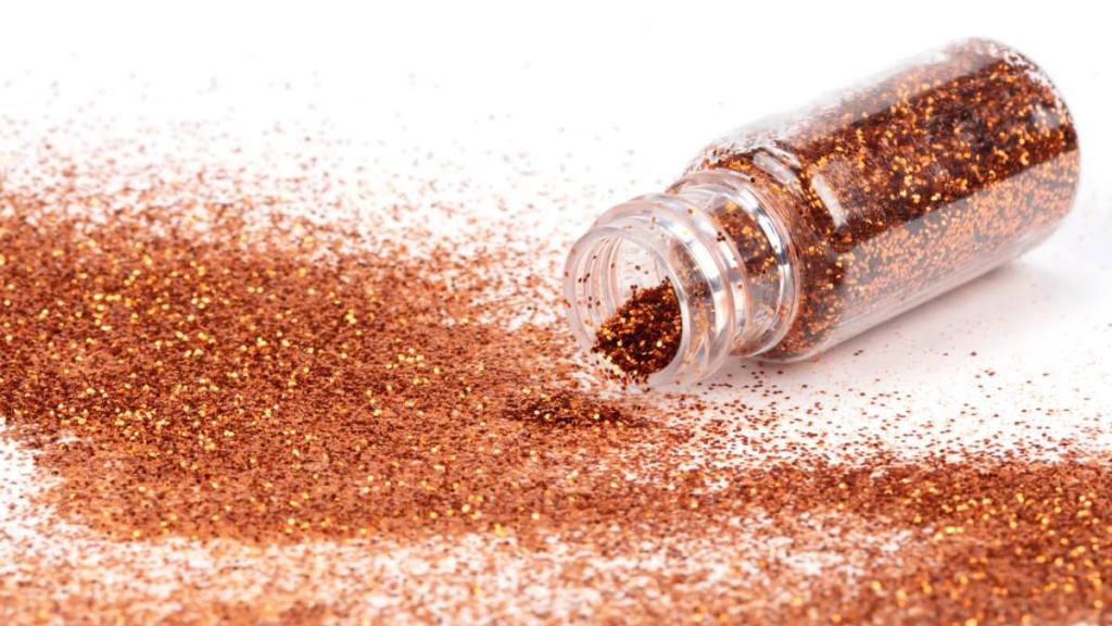 How to clean up glitter: Gold sparkles pour out of the bottle. Glitter is pouring from a bottle on a white background