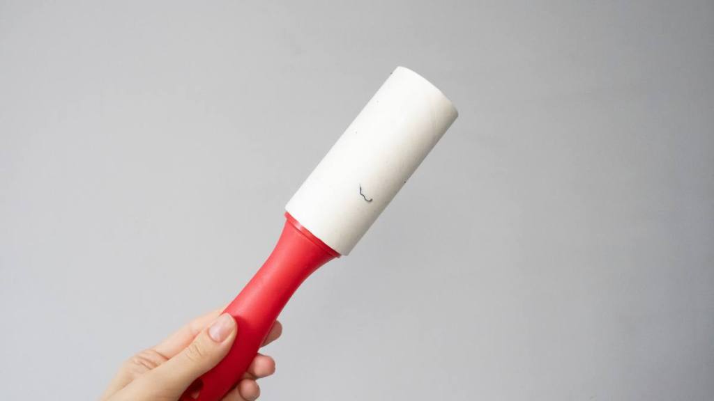 How to clean up glitter: A woman's hand holds a used sticky roller against a gray background