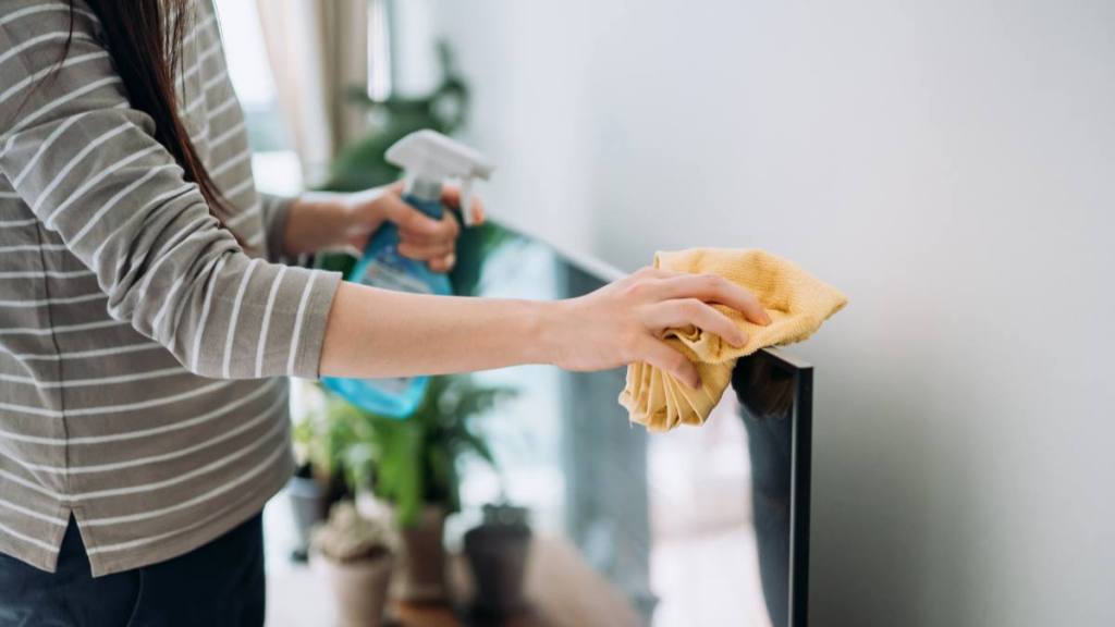 How to clean a TV screen: Cropped shot of a young woman cleaning the surface of a TV with cleaning spray and antistatic cloth at home during the day