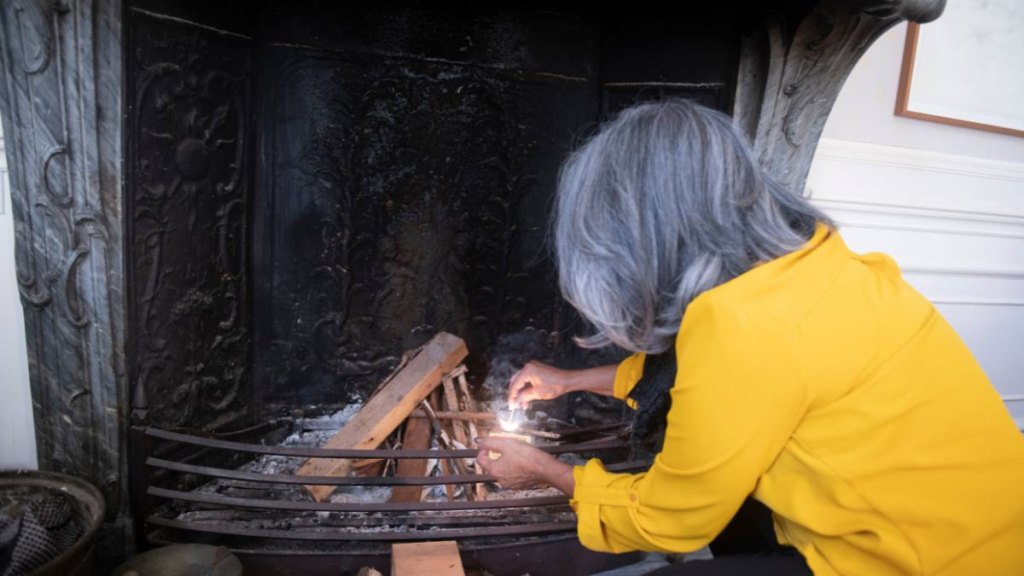 Senior woman lighting the fireplace for a gathering with friends