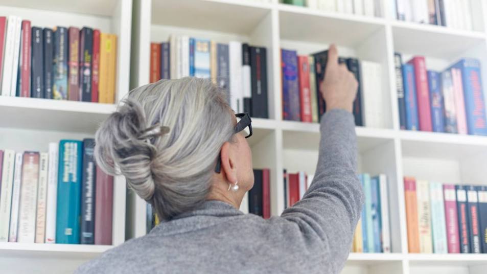 Bookshelf organization: Senior woman taking book from bookshelf, rear view