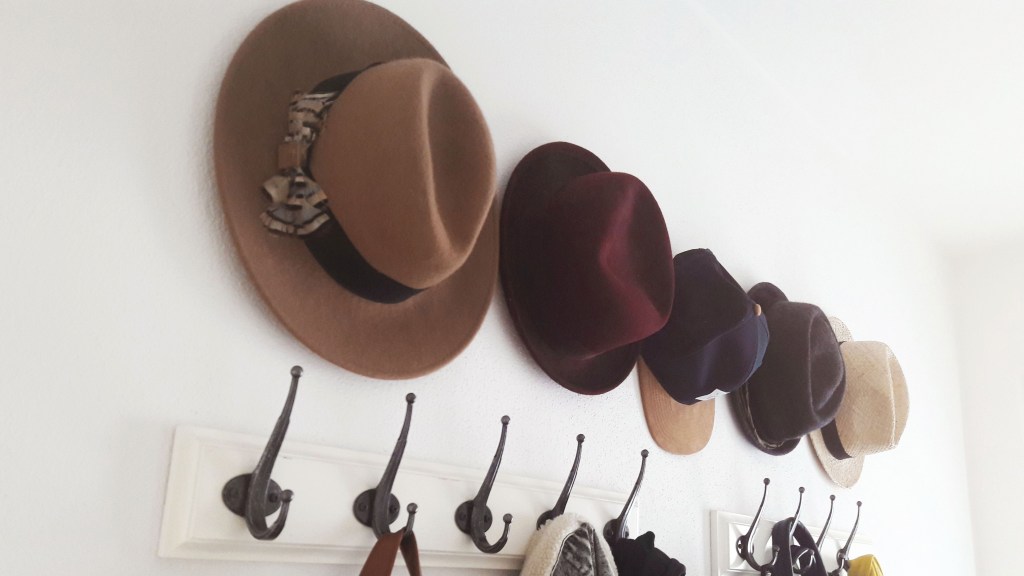 How to organize winter hats and gloves: Wide-brim hats and ballcaps hung from sticky hooks in a row on a wall