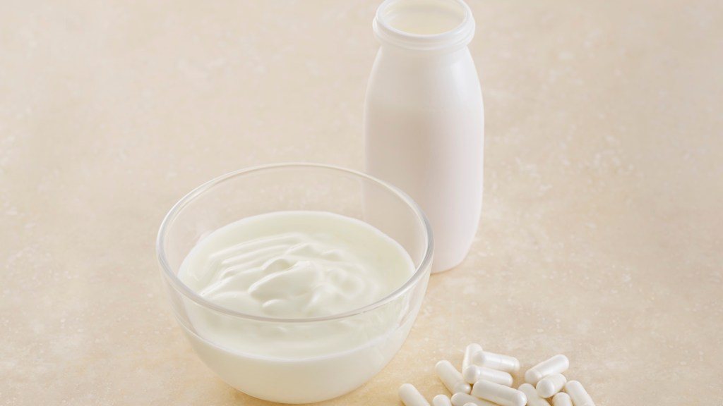 Probiotic pills next to a bowl of probiotic-filled yogurt and bottle of milk, which is beneficial for skin health