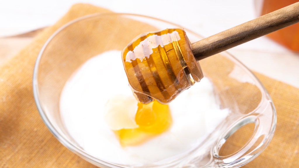 Honey dipper drizzling honey into a small bowl of Greek yogurt