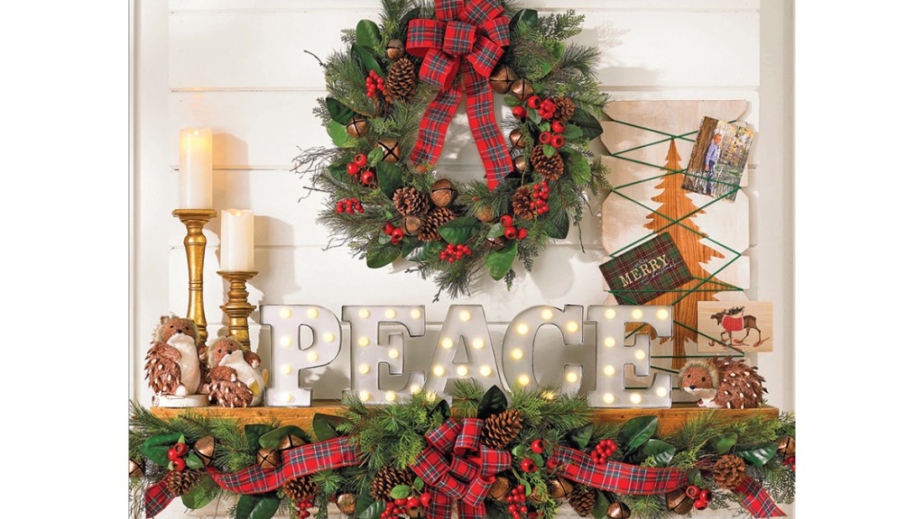 Christmas mantel ideas: Farmhouse chic mantel featuring a greenery garland and wreath kissed with berries and plaid ribbon, a marquee sign that spells "peace", candlesticks and a Christmas card holder on wood mantel