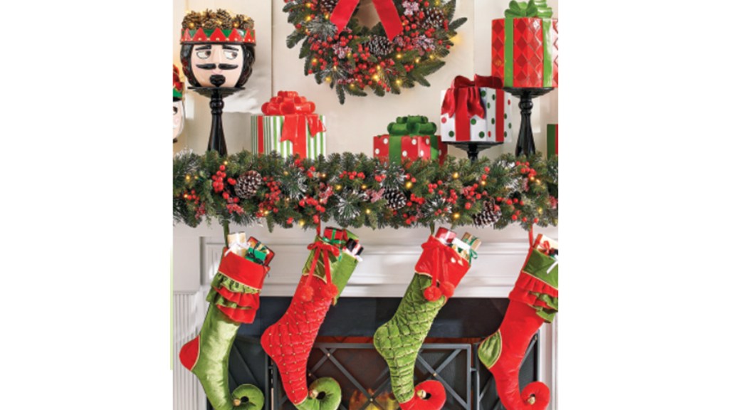Christmas mantel ideas: Whimsical mantel with greenery garlands, wrapped presents and a nutcracker head plant pot on pedestals and elf shoe stockings on white mantel.