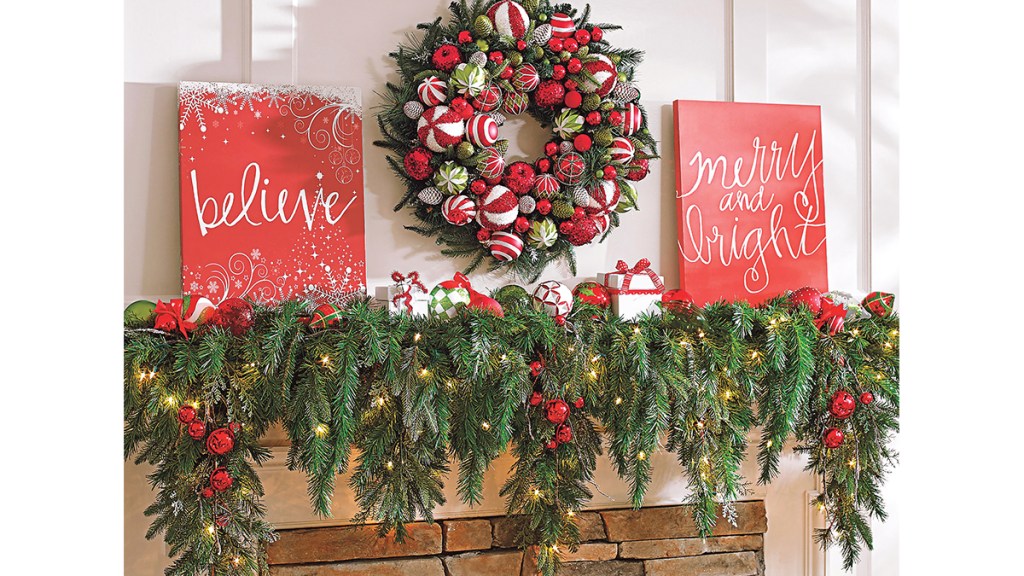 Christmas mantel ideas: Merrily modern mantel featuring a cascading greenery garland, a bauble-kissed wreath, red canvas artwork, ornaments and bitty wrapped presents on a wood mantel