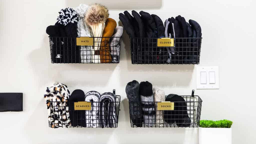 How to organize winter hats and gloves: Hats, gloves, scarves and socks folded and sorted into four metal baskets hanging on an entryway wall