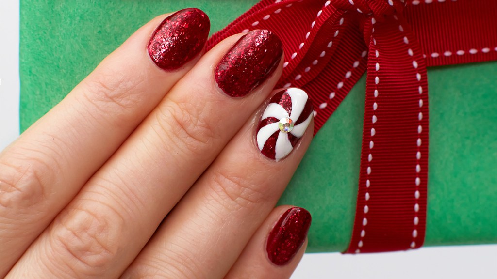 Nails painted with sparkly red polish and a peppermint swirl accent nail, one of the holiday nail ideas