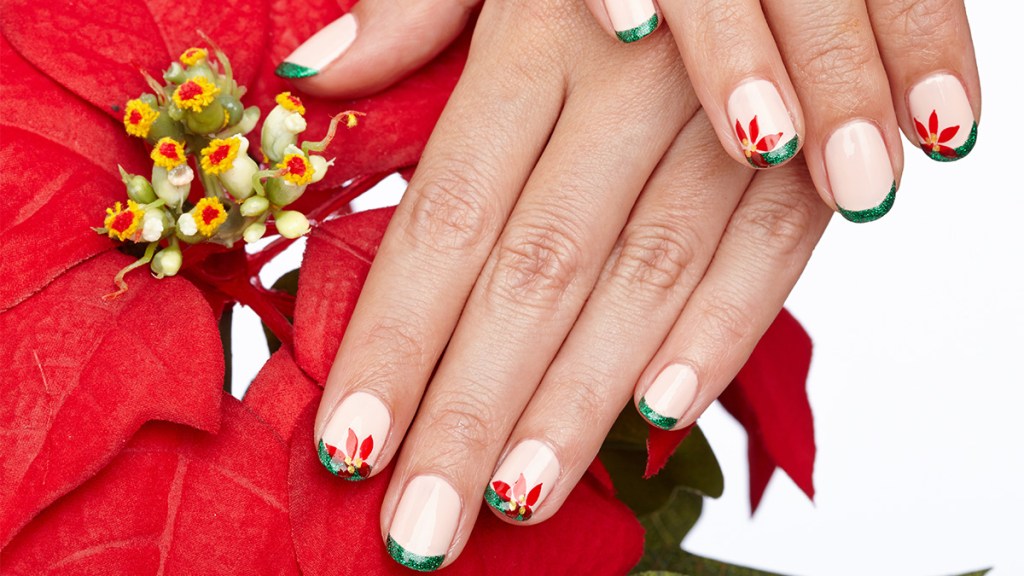 Nails painted with a light pink base color and green French tips with poinsettia flower accents, one holiday nail ideas