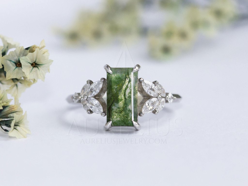 Next on the list is Heptagon Moss Agate and Diamond Ring which effortlessly combines an unusual geometric stone setting and classic side diamonds. 7-sided gemstones are not something you see often so one could say this is your lucky day!
Even though a baguette cut can be considered a hybrid between a classic and geometric stone cut, we felt the need to include it on the list. This Aurelius Baguette Moss Agate Engagement Ring is flanked by marquise diamonds resembling leaves for a beautiful nature-inspired look.