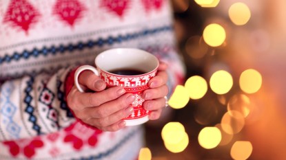 Woman's hands holding mug with Christmas lights in background