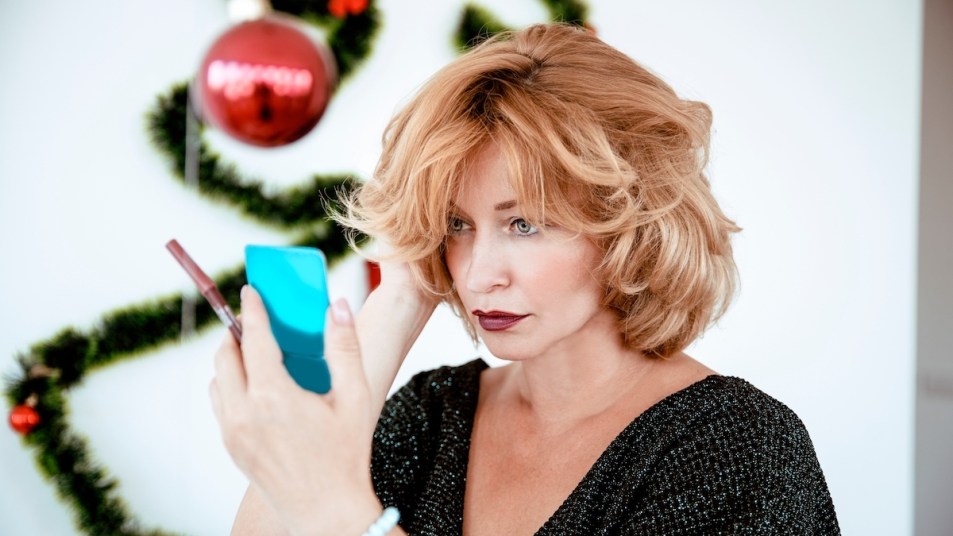 Woman adjusting hair and looking in mirror with holiday decor in background