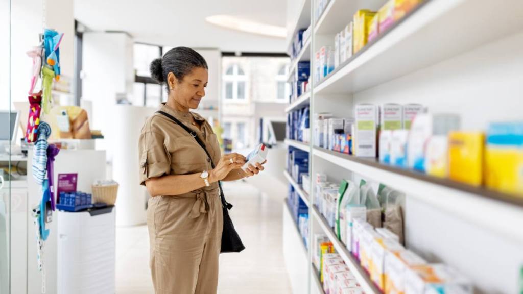 How to prevent a cold when you feel it coming: Female customer picking and looking at the medicine box from the shelf. Senior woman buying medicine at drugstore.