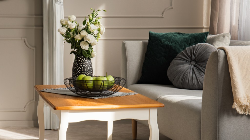 How to decorate a coffee table: Wooden coffee table decorated with a black metal bowl filled with green apples and a black and white vase filled with white ranunculus 