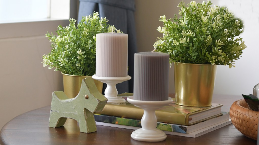 How to decorate a coffee table: Round wooden coffee table topped with a stack of books, pedestal candle holders, gilded plant pots and a wooden dog figurine 