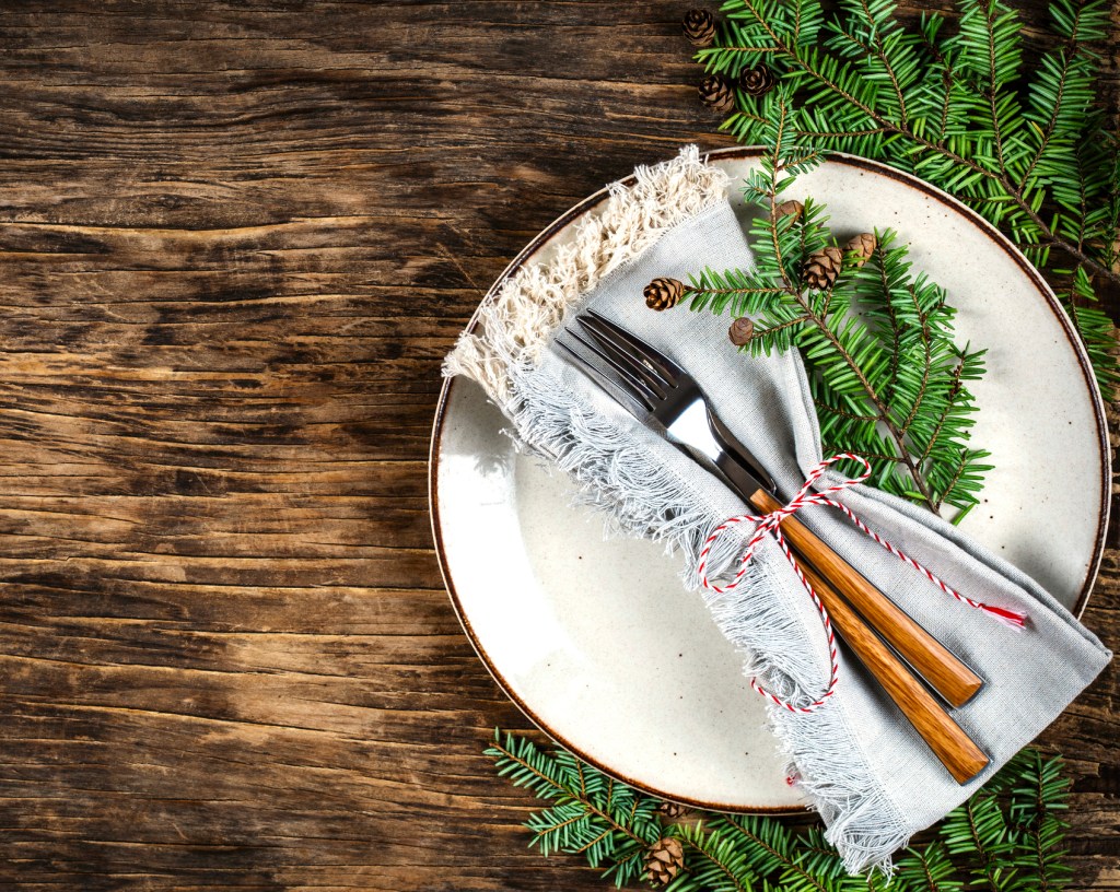 Winter brunch ideas: Table setting with plate, fork, knife and branches of fir with pine cone, space for text on wooden background